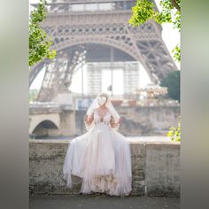 a woman in a wedding dress sitting on a wall near the eiffel tower