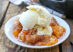 a white plate topped with fruit cobbler and ice cream on top of a wooden table