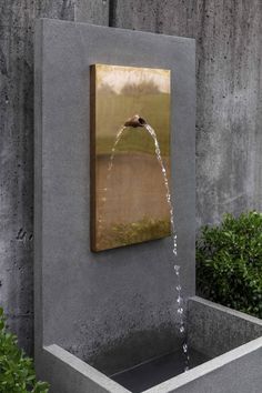 a water fountain is shown in front of a wall with plants and bushes around it