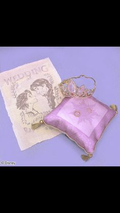 a pink pillow with a tiara on it next to a purple and white handkerchief