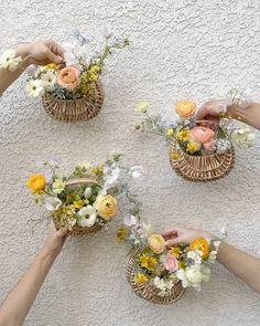 four baskets filled with flowers on top of a white wall next to two hands reaching for each other