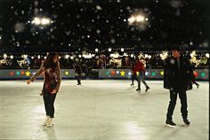 people skating on an ice rink at night with lights and snow flakes in the background