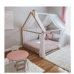 a white canopy bed sitting in a bedroom next to a pink table and small chair