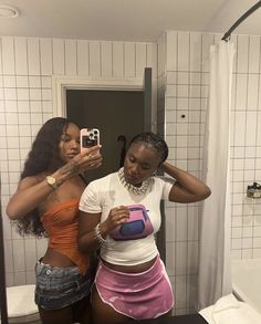 two women in a bathroom looking at their cell phones and taking pictures with each other