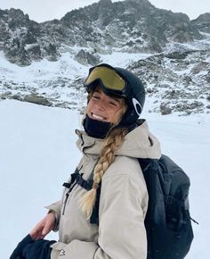 a woman with long braids and ski goggles smiles while standing in the snow