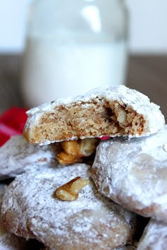 a pile of powdered sugar covered doughnuts next to a glass of milk