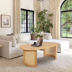 a living room with white furniture and large windows in the back ground, there is a coffee table on top of a beige rug