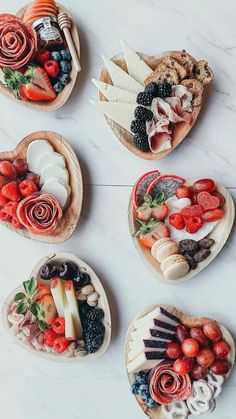 four wooden heart shaped bowls filled with fruit and veggies on top of a white table