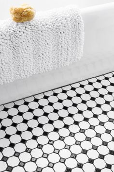 a teddy bear sitting on the edge of a bathtub with black and white tiles