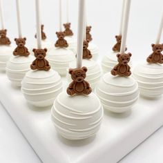 there are many white cake balls with brown teddy bears on them and candles in the middle