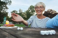 an older woman sitting at a picnic table holding out her hand