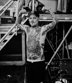 a man with tattoos standing in front of some stairs and holding his arms above his head