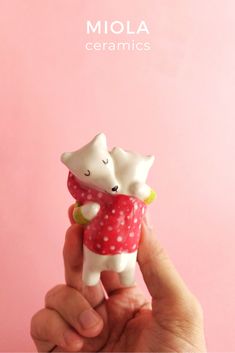 a hand holding a small figurine with two cats on it's back