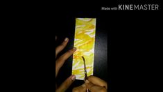 two hands holding scissors in front of a piece of paper with yellow paint on it