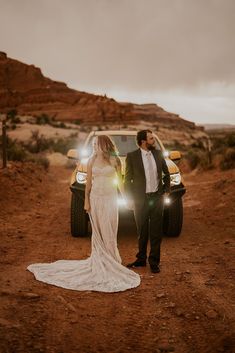 a bride and groom standing in front of a truck with their lights on at sunset