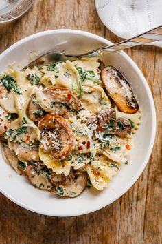 pasta with mushrooms, spinach and parmesan cheese in a white bowl on a wooden table