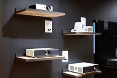 some shelves with electronic equipment on them in a store or showroom, including a projector and other items