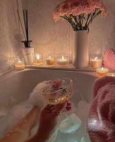 a woman in a bathtub holding a glass of wine with candles on the side