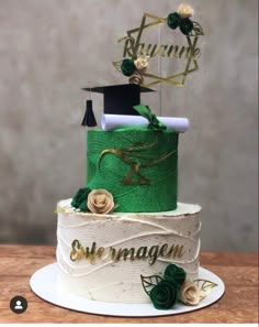 a three tiered cake decorated with green and gold ribbons, topped with a graduation cap