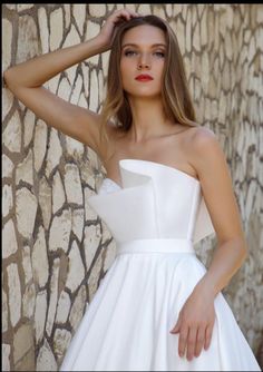 a woman in a white dress posing for the camera with her hand on her head