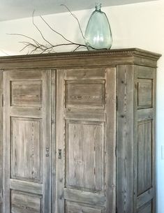 an old wooden armoire with two doors and a glass vase on top of it