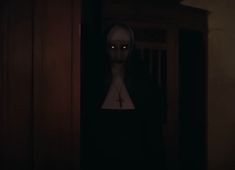 a creepy figure standing in front of a door with red eyes and a cross on it's chest