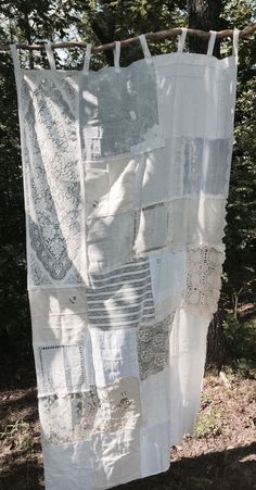 a white quilt hanging from a clothes line in the woods with trees behind it and sun shining through