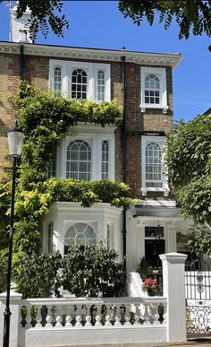 a large house with many windows and plants on the front porch, along with a white picket fence