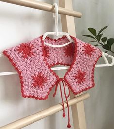 a pink crocheted top hanging on a clothes rack next to a potted plant