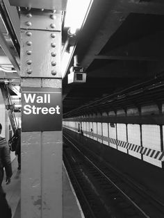 two people are standing next to a wall street sign at the subway station in new york city