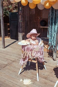 a baby sitting in a highchair with balloons and decorations on the ground next to it