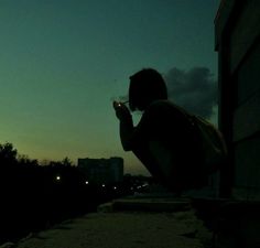 a person sitting on a ledge looking at their cell phone in the dark with buildings in the background