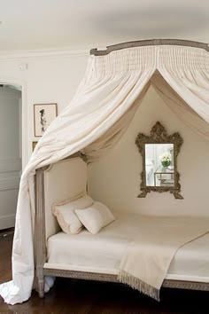 a canopy bed with white sheets and pillows on top of it, in a bedroom