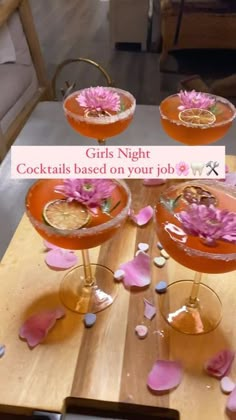 four cocktail glasses filled with pink flowers on top of a wooden table