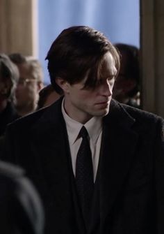 a young man in a suit and tie standing next to other people looking at something