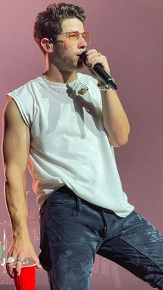 a male in a white shirt is holding a red cup and singing into a microphone