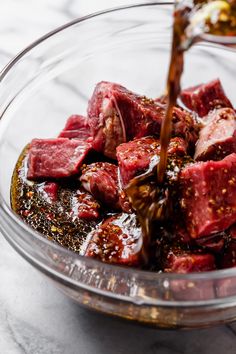 a bowl filled with meat and seasoning being poured into it