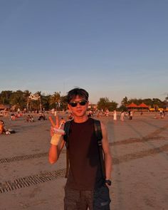 a man standing on top of a sandy beach holding two fingers up in the air