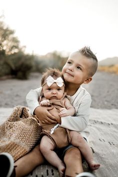 two young children sitting on the ground with their arms around each other and smiling at the camera