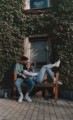 a man and woman sitting on a bench in front of a building with ivy covered walls