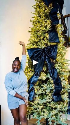 a woman standing in front of a christmas tree holding her arms up to the sky