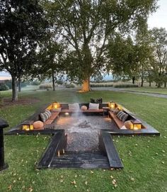 a fire pit in the middle of a grassy area with benches and lights on it