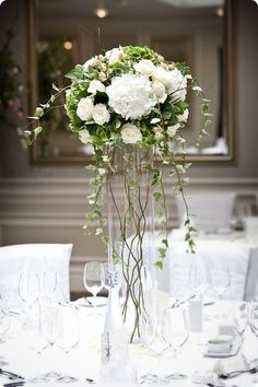 a vase filled with white flowers sitting on top of a table next to wine glasses