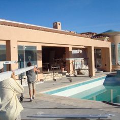 two people are moving furniture around the pool area in front of a house that is under construction