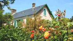 a pink house with green shutters and flowers in the foreground, surrounded by greenery