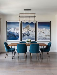 a dining room table with blue chairs and pictures hanging on the wall above it in front of a fireplace