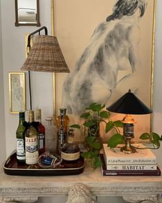 a table topped with bottles of alcohol and a lamp next to a painting on the wall