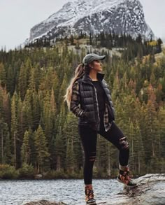 a woman standing on top of a rock next to a lake