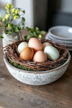 four eggs in a bird's nest sitting on a table next to plates and flowers