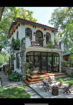 a large white house with lots of windows and plants on the front porch, surrounded by greenery